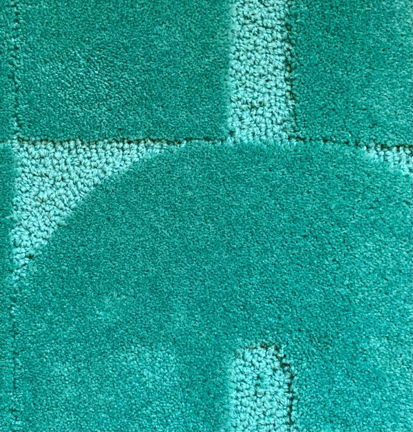 Zoom sur le tapis en laine vert. Le tapis a un style seventies. Le tapis made in france est fait main. Le tapis est en laine verte. Il y a un mélange de laine bouclée et laine velours ce qui lui donne un côté texturé, géométrique et contemporain